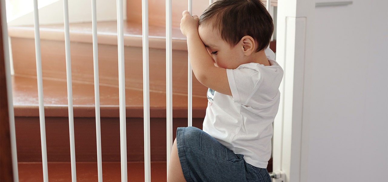 Baby kneeling and holding onto a baby gate near the stairs