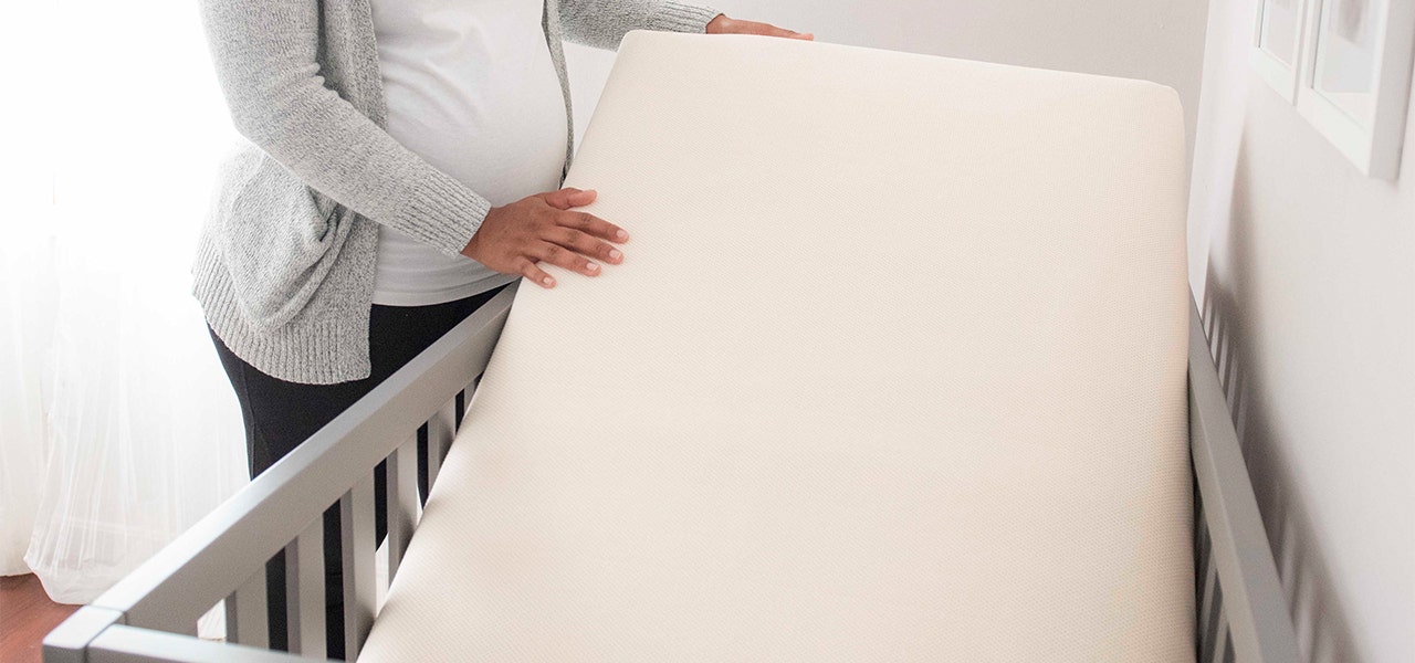 Pregnant parent lifting a lighweight waterproof crib mattress
