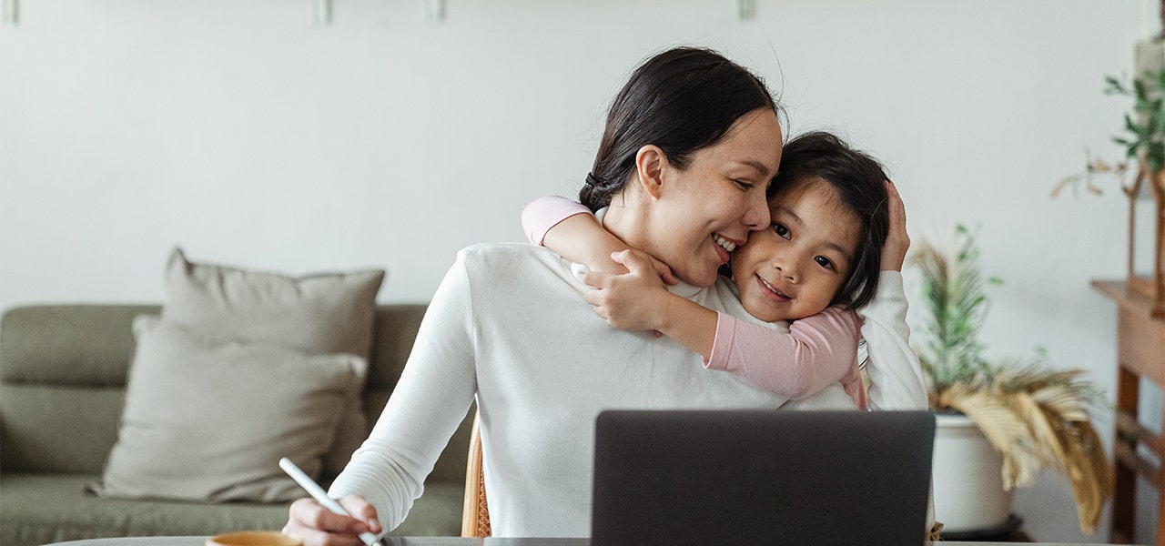 Mother and child hugging, while mother researches on a laptop