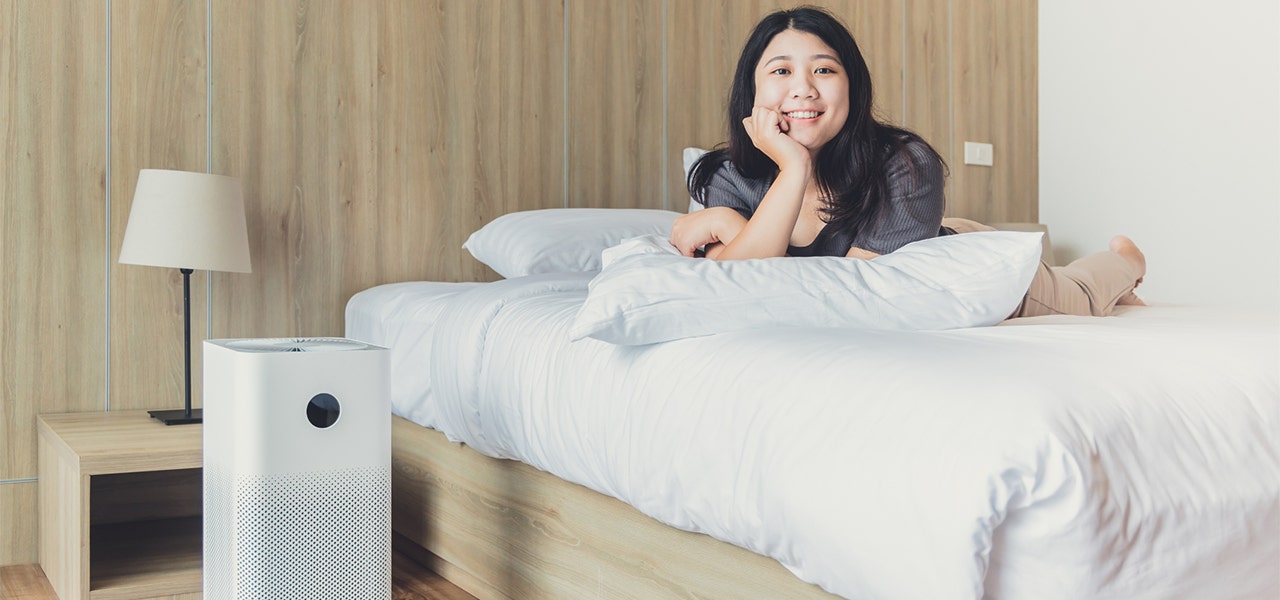 Woman relaxing on her bed with an air purifier nearby