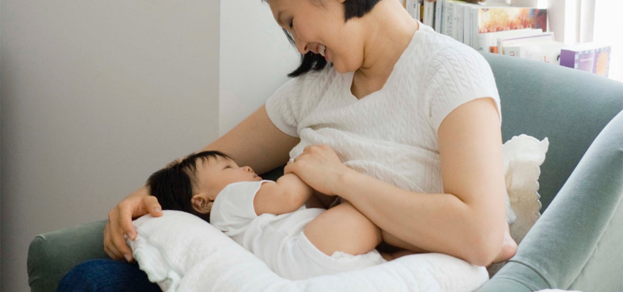 Mother in a comfy chair breastfeeding her baby with the help of a nursung pillow