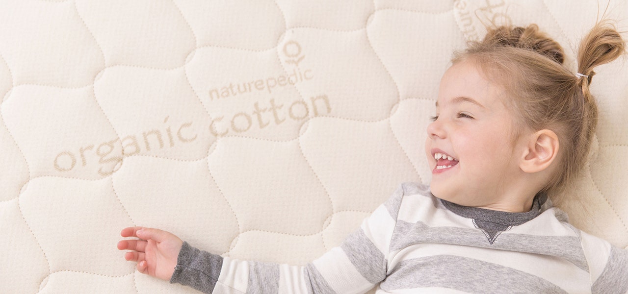 Preschool-aged girl lying down and laughing on a Naturepedic organic kids mattress