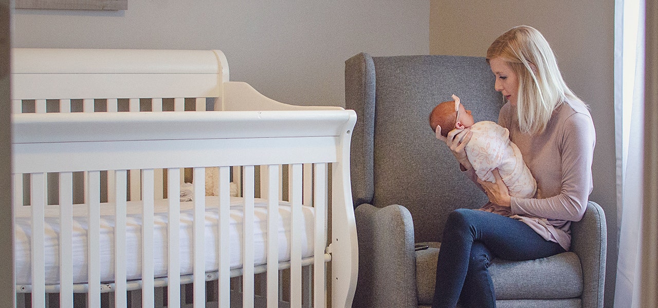 Mother holding newborn on a chair in the nursery