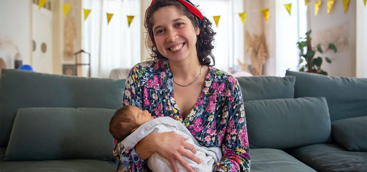 Smiling mother sitting on the couch and holding her sleeping infant