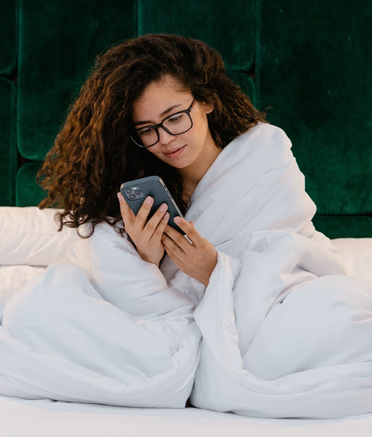 Woman wrapped in a plush duvet and looking at her phone