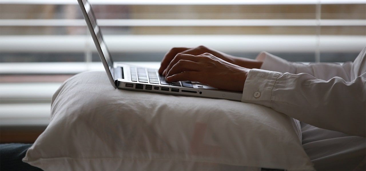 Person researching on a laptop restng on a pillow