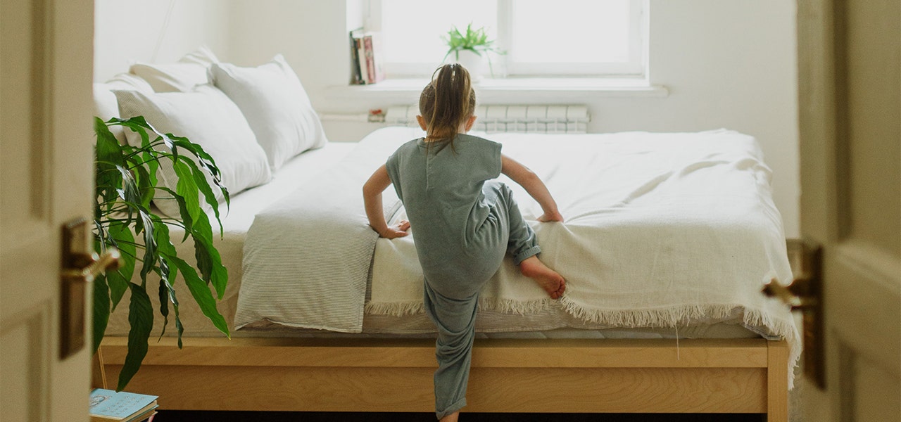 School-aged girl climbing into bed in a healthy organic sleep environment