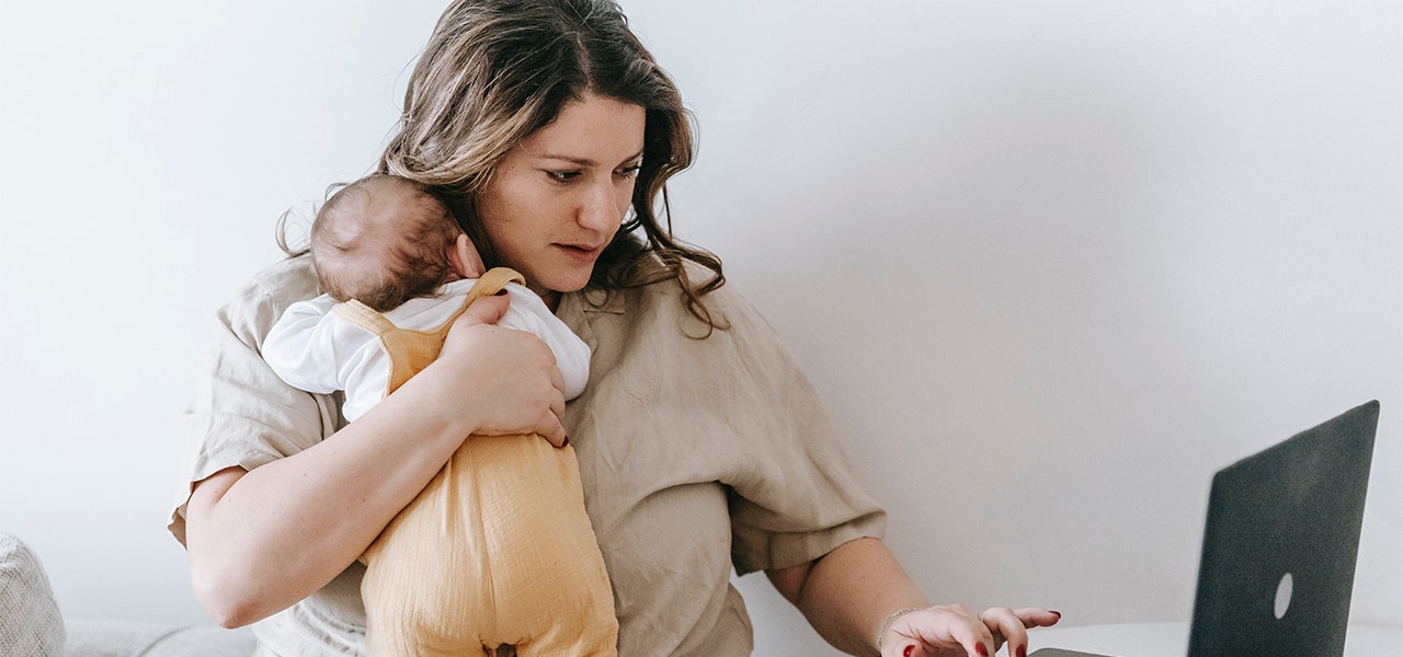 New mom holding her baby and working on a laptop