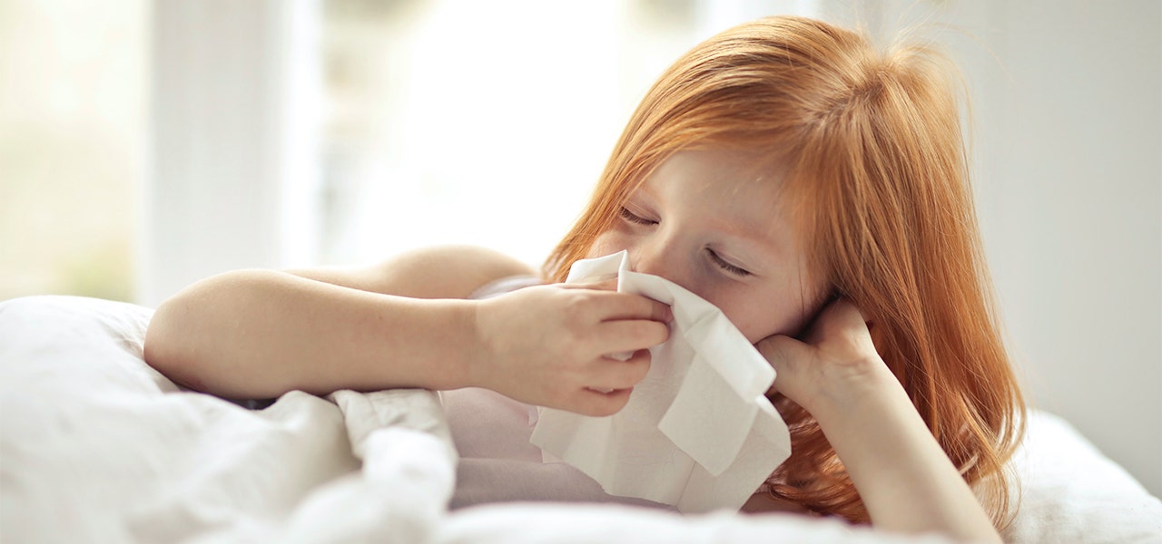 Child lying in bed and sneezing into a tissue