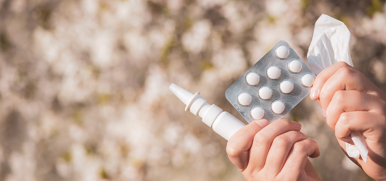 Person holding kleenex and allergy medications