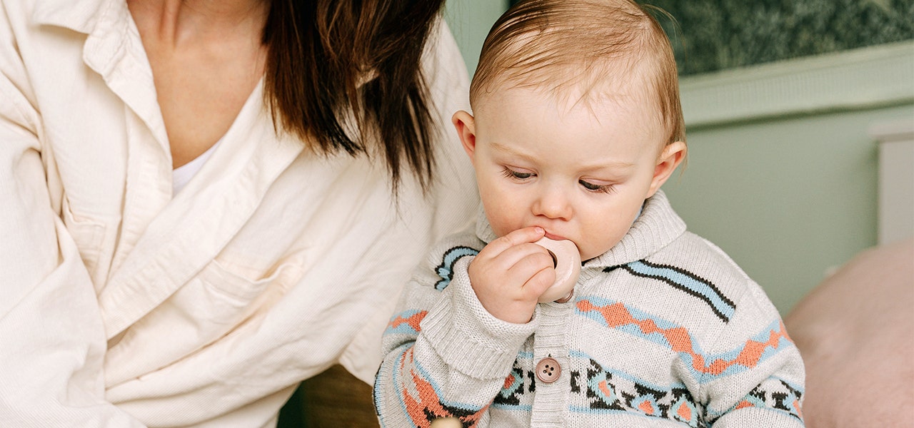 Mother holding a baby who us using a teething toy