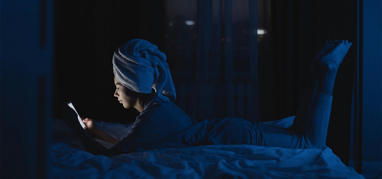 person with hair wrapped in towel laying in bed on cell phone