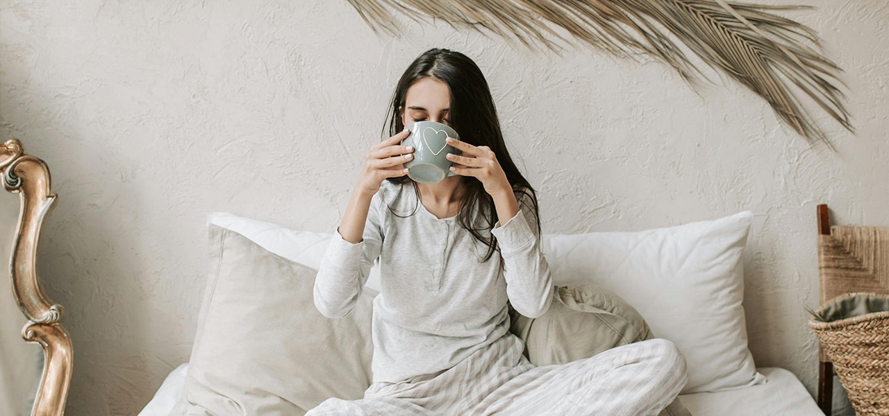 woman sipping from mug in bed