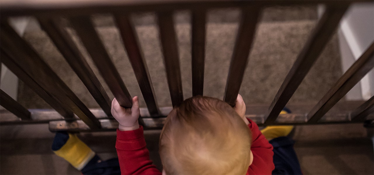 child looking through the bars of a baby gate over stairs